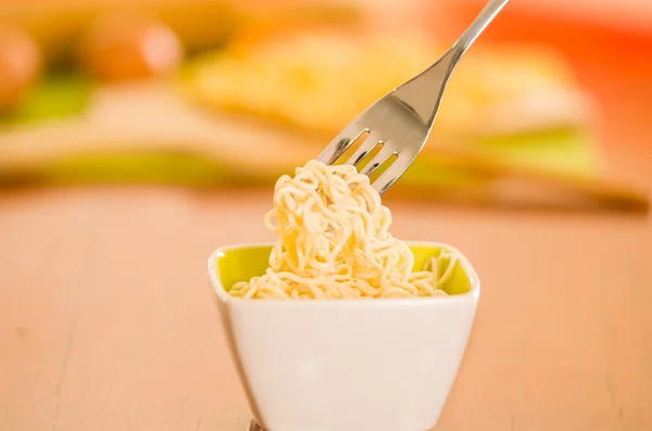 Κομψή παρουσίαση του μαγειρευμένα noodles μέσα στο μικρό τετράγωνο μπολ κάθεται σε ξύλινη επιφάνεια, αρπαγή τροφίμων για πιρούνι, θολή φόντο — Φωτογραφία Αρχείου