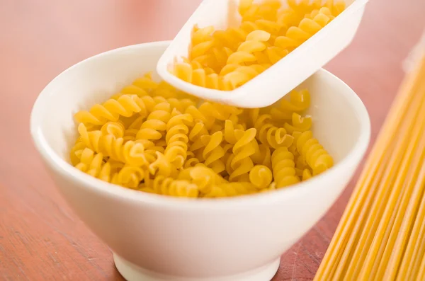 Large kitchen spoon grabbing dry fusilli out from white bowl, professional setting — Stock Photo, Image