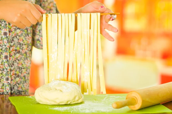 Spaghetti freschi fatti appesi attraverso bastone di legno tenuto da donna , — Foto Stock
