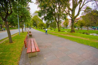 Cuenca, Ekvator - 22 Nisan 2015: Uzun boylu ağaçlar her iki tarafta huzurlu yürüyüş ve bisiklet avenue boyunca ahşap Bank