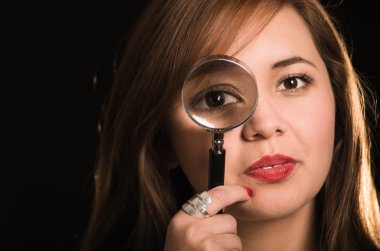 Genç kadın sağ gözü gelişmiş efekti, siyah arka plan üzerinde büyüteç tutarak kamera karşı karşıya