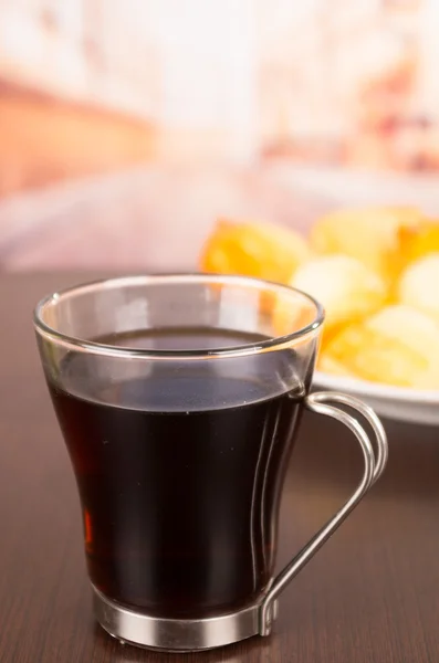 Little cup with coffee and metal handle on table, blurry plate of food in background — Stock Photo, Image