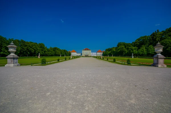 Nymphenburg, Niemcy - 30 lipca 2015: Piękny pałac jak widać z odległości z rzeźbami po obu stronach alei prowadzącej do budynku — Zdjęcie stockowe