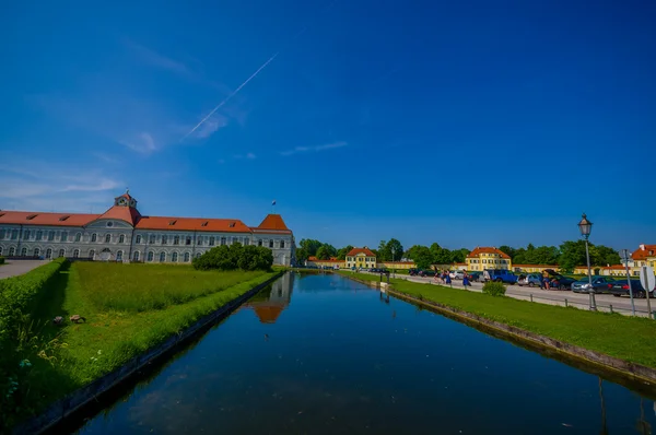 Nymphenburg, Tyskland - 30 juli, 2015: Idylliska del av slottsträdgården med lugna blå floden kanal och stora byggnader i bakgrunden — Stockfoto