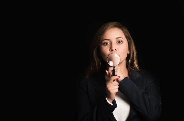 Young woman standing wearing casual clothes, holding magnifying glass with one hand looking towards camera — Stock Photo, Image