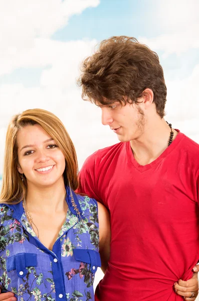 Junges Paar zeigt seine Liebe zur Kamera, posiert vor Strandhintergrund, Mann mit rotem Hemd und Jeans, Mädchen trägt blaues Kleid — Stockfoto