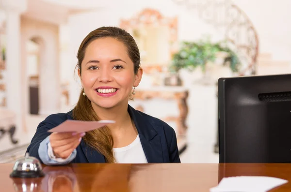 Jeune brune réceptionniste d'hôtel avec sourire amical remettre la clé au client à travers le bureau, point de vue des clients — Photo
