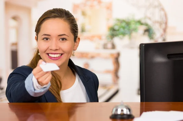 Unga brunett hotellreceptionist med vänliga leende lämnar över nyckeln till klienten över skrivbord, kunder synvinkel — Stockfoto