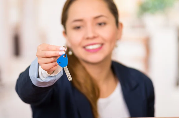 Young brunette hotel receptionist with friendly smile handing over key to client across desk, customers point of view — Stock Photo, Image