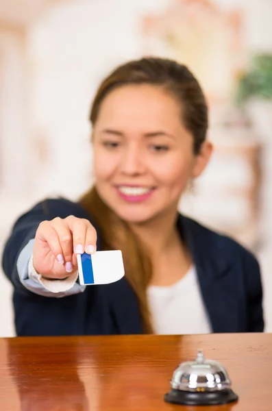 Jovem morena recepcionista do hotel com sorriso amigável entregando a chave ao cliente em toda a mesa, o ponto de vista dos clientes — Fotografia de Stock