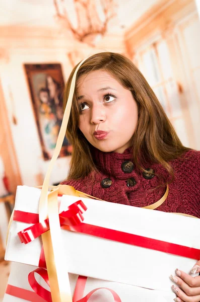 Brünette mit schönem Lächeln hält Geschenk glücklich posiert für die Kamera, weiße Verpackung und rote Schleife, Haushalt Hintergrund — Stockfoto
