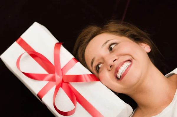 Primo piano bruna headshot come visto dall'alto, grande sorriso e testa a riposo accanto a presentare con carta bianca avvolgente nastro rosso — Foto Stock