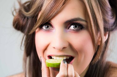 Headshot esmer, koyu mystique göz ve yeşil ruj, kameraya bakarken kireç dilim üzerinde ısırma