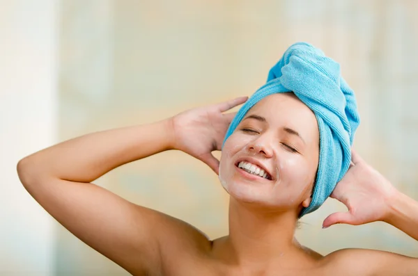 Mooie jonge gezonde Spaanse vrouw headshot met naakte schouders, blauwe handdoek gewikkeld rond hoofd, gelukkig, poseren, romige handen en ogen dicht — Stockfoto