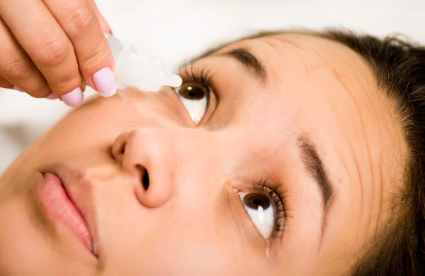 Closeup headshot young woman lying down, hand holding eye drops bottle above womans open eyes