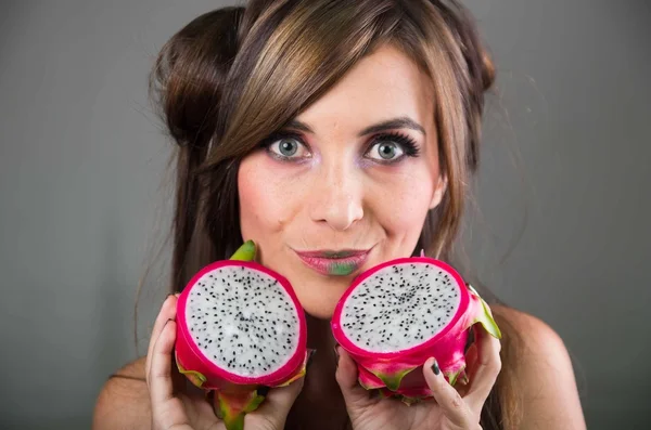 Headshot brunette, donkere mystique look en groene lippenstift, bedrijf in twee openen helften van roze pitaya fruit met beide handen geconfronteerd met camera — Stockfoto