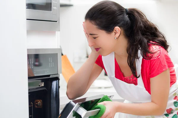 Chef van de jonge vrouw op zoek naar oven met gefrustreerd gelaatsuitdrukking — Stockfoto