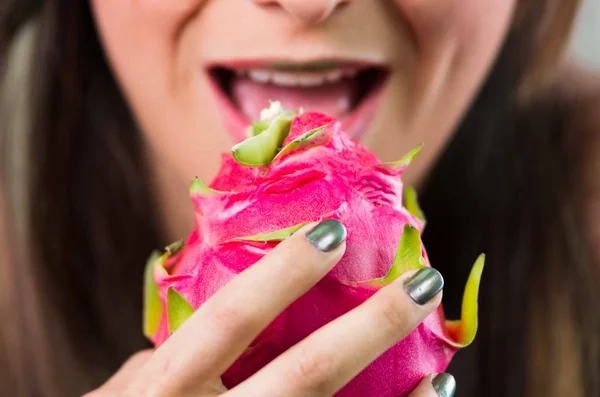 Cabeza morena, mirada mística oscura y lápiz labial verde, sosteniendo fruta pitaya rosa con ambas manos frente a la cámara — Foto de Stock
