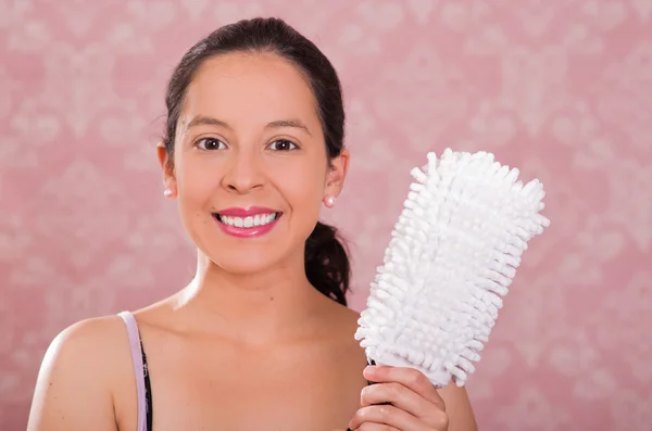 Brunette woman holding white fluffy cleaning brush while smiling to camera, pink background — Stock Photo, Image