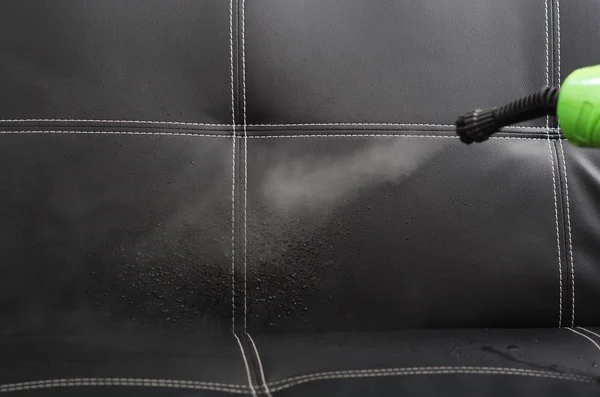 Closeup steam exiting nozzle of vapor cleaning machine, rinsing black leather couch — Stock Photo, Image