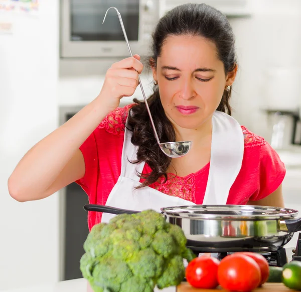 Giovane donna chef degustazione di cibo da bollitore con espressione facciale scettica — Foto Stock