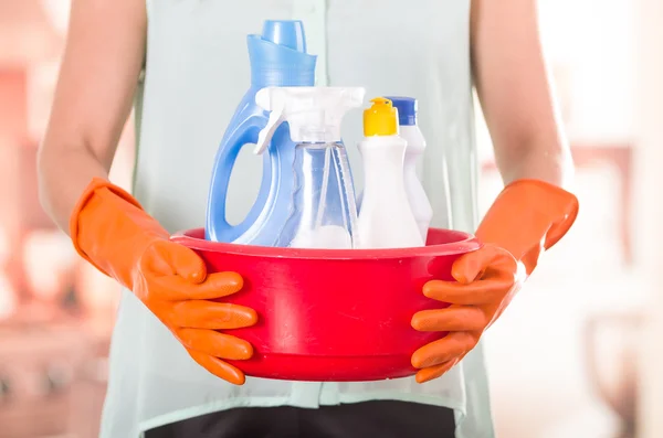Closeup oranje handschoenen houden rode emmer reinigingsproducten en lacht om camera, housecleaning concept — Stockfoto