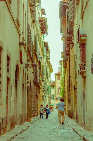 FLORENCE, ITALY - JUNE 12, 2015: Unidentified people walking into a pinturesque street, old historic buildings on the sides with windows and balconies.