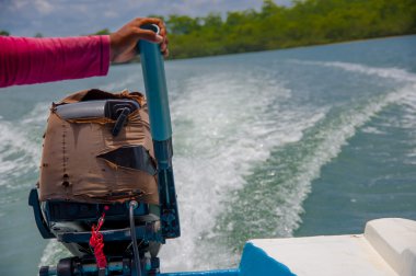 Muisne, Ecuador - March 16, 2016: Arm holding onto boat engine, wave trace visible on water from driving, great perspective and beautiful colours