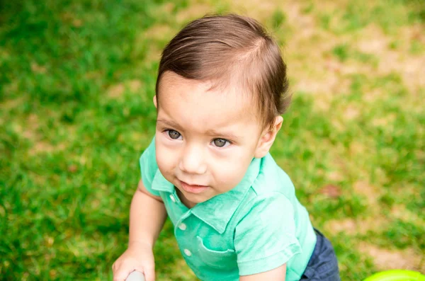 Carino il bambino che indossa t-shirt turchese e capelli pettinati, seduto fuori sulla superficie erbosa giocando intorno — Foto Stock