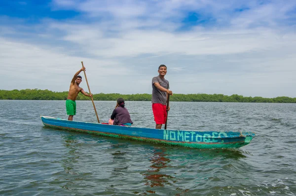 Muisne, Ecuador - March 16, 2016: Two people standing inside green canoe while one more person sitting down, out on pacific ocean, beautiful forest coastline background — Stock Photo, Image