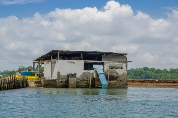 Muisne, Equador - 16 de março de 2016: Edifício industrial de concreto pequeno sentado na margem do rio com tubulação azul conectada à água do oceano — Fotografia de Stock
