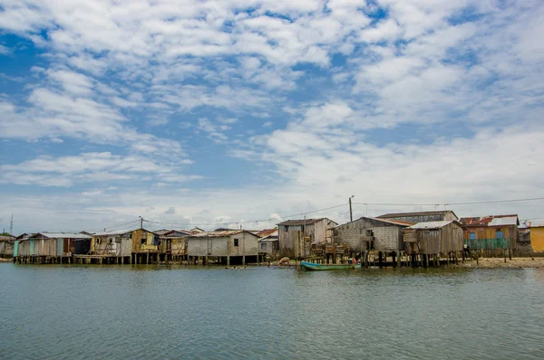 Muisne, Equador - 16 de março de 2016: Muisne cidade vista da água, modestas casas de madeira sentadas em postes à beira-mar oceano pacífico, prédios da cidade fundo e belo céu azul — Fotografia de Stock