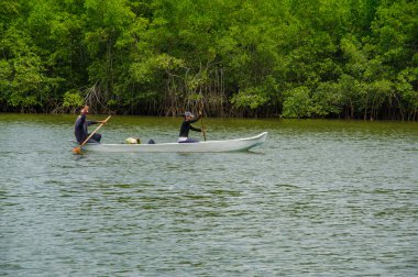 Muisne, Ekvator - 16 Mart 2016: Adam ve küçük Kano kıyı, arka planda ağır yeşil bitki örtüsü yanında kürek çekmeye içinde oturan kadın