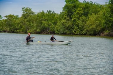 Muisne, Ekvator - 16 Mart 2016: Adam ve küçük Kano kıyı, arka planda ağır yeşil bitki örtüsü yanında kürek çekmeye içinde oturan kadın