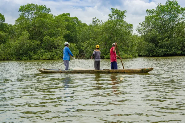 Muisne, Ecuador - March 16, 2016: Three guys fishing using net close to shore from wooden traditional canoe with green trees background — Stock Photo, Image