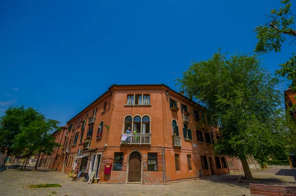 MURANO, ITALIA - 16 DE JUNIO DE 2015: Casa naranja en la esquina de la calle Murano, gente en el balcón y un pequeño mercado abajo — Foto de Stock