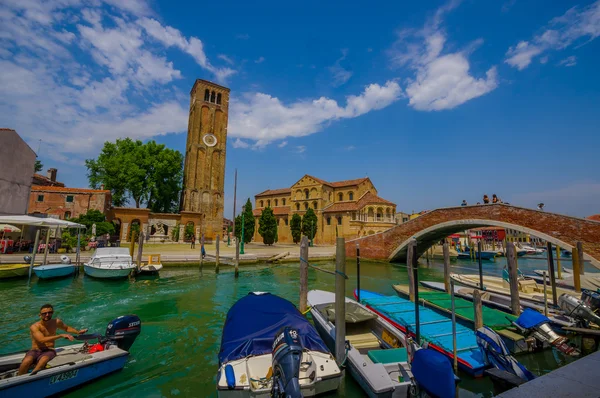 Murano, Italië-16 juni 2015: kathedraal van Muranos en uitzicht op de toren vanaf de andere kant van het kanaal, boten parkeren en mooie bakstenen brug aan de zijkant — Stockfoto