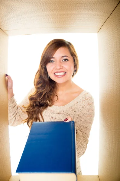 Lächelndes Mädchen in der Schachtel, das mit einer Hand ein blaues Buch hält und mit der anderen einen Schachtelrand — Stockfoto