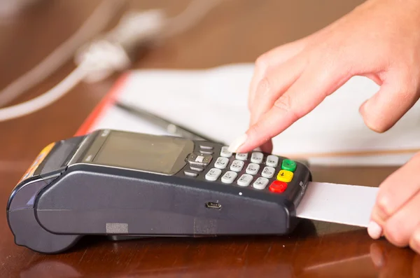 Eine Frau bedient einen Kreditkartenautomaten, wobei die Karte unter dem Automaten eingegeben wird und ein Finger auf einen Boden drückt — Stockfoto