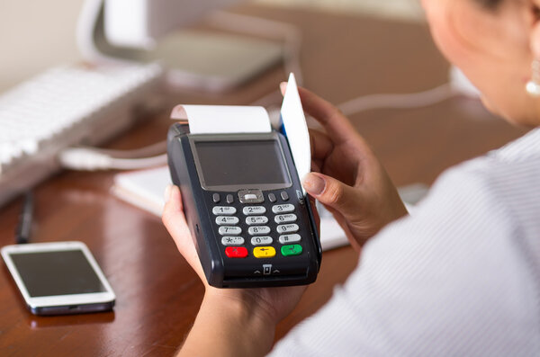 Close up of a person swiping a credit card in a machine, behind a table with a mobile phone