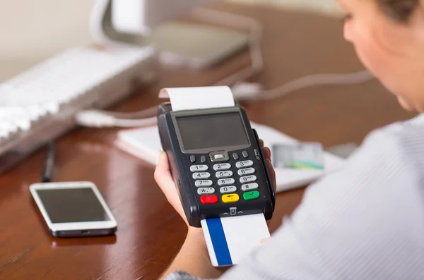 Eine Frau, die mit einer weißen und blauen Kreditkarte bezahlen will, Karte in einem Automaten. auf einem Tisch ein Handy und ein Computer — Stockfoto