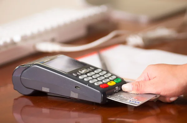 Credit card terminal on a wooden table, visa card entering under this. Behind paper and computer — Stock Photo, Image