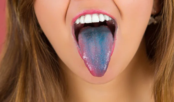 Primer plano de una mujer con la boca abierta extendiendo la lengua de color azul con fondo rosa —  Fotos de Stock