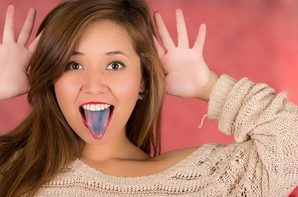 Mujer con la boca abierta extendiendo la lengua de color azul con fondo rosa y la mano abierta con los dedos en la cabeza —  Fotos de Stock