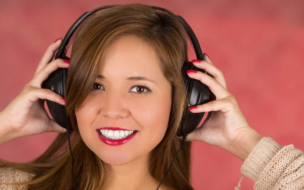 Joyeux visage femme avec les mains sur les écouteurs, fond rose — Photo