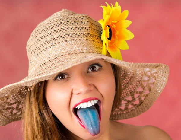Woman sticking out her blue tongue with a nice beige hat with a sunflower on it — Stock Photo, Image