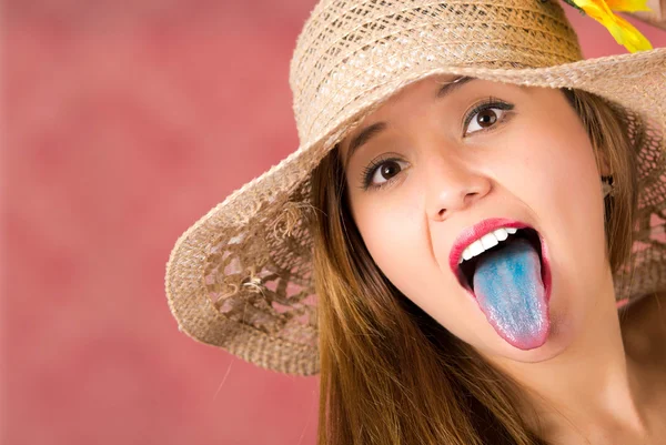 Leuk meisje krijgt wat leuks met blauwe tonge uitsteekt en leuke hoed op een roze achtergrond — Stockfoto