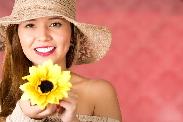 Vrouw houden een zonnebloem met haar handen, een hoed in haar hoofd en het glimlachen op een roze achtergrond — Stockfoto