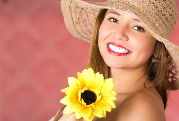 Mujer sonriente y feliz con un sombrero en la cabeza y sosteniendo un girasol. Hombro desnudo en un fondo rosa — Foto de Stock