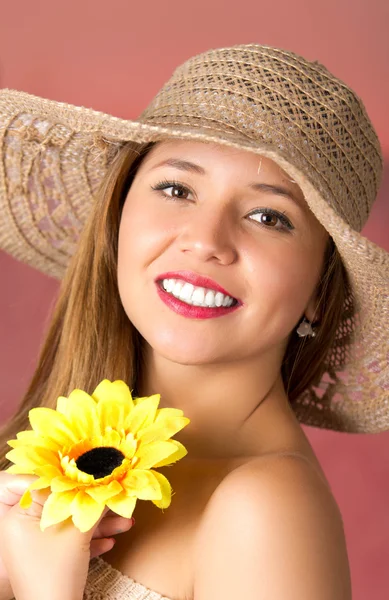 Mulher smailing e feliz com um chapéu em sua cabeça e segurando um girassol. Ombro nu em um fundo rosa — Fotografia de Stock